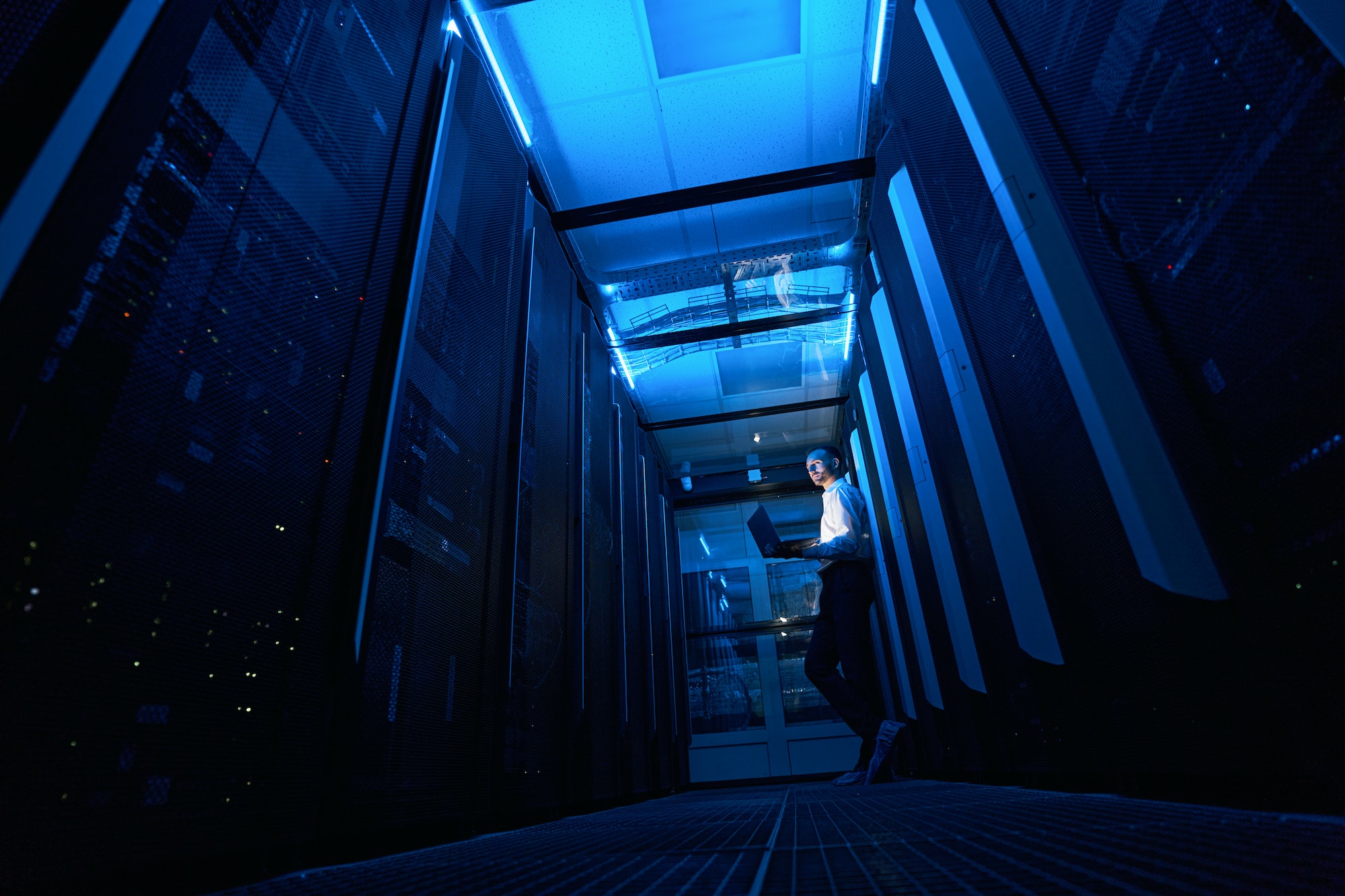 Man network administrator with laptop leaning against server rack